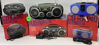Five portable boomboxes displayed on original boxes with power cords, showing varied designs and colors