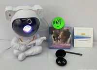 White astronaut LED lamp with guitar and glowing colorful light in visor alongside Kaucic noise cancelling earbuds, charging case, and packaging.