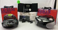 Shows entire lot of audio equipment with boxes - two boomboxes, Bluetooth CD micro system, remote and power cords