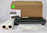 Photo showing FoodSaver FM2000 vacuum sealer with two sealer rolls, vacuum seal bags, owner's manual, and cardboard box.