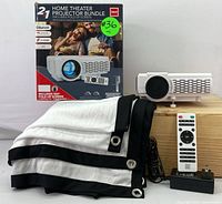 Full set showing RCA projector, remote control, power adapter, fold-up screen, and original packaging box for the home theater projector bundle.