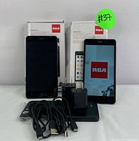 Two RCA 5.5-inch smartphones with original boxes, chargers, cables, and phone stands. One phone powered on showing RCA logo, the other phone screen off.