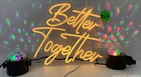 LED "Better Together" neon sign illuminated with two multicolor party lights projecting colored spots on wall and table