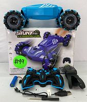 Blue stunt climbing car resting on packaging box with remote control, rechargeable battery, USB charging cable, and charger adapter shown in front