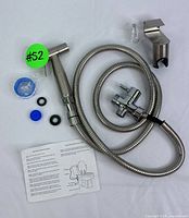 Full bidet sprayer set laid out showing handheld nozzle, flexible hose, T-valve adapter, wall mount holder, washers, tape and instruction manual.