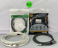 Photo showing the 8K HDMI cable sealed in its packaging with specifications visible, UGREEN USB cable in packaging, and two coiled white charging cables with black velcro ties.