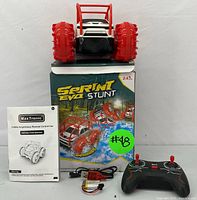 Photo showing the stunt car on top of original box, with remote control, rechargeable battery, USB charging cable, and instruction manual laid out.