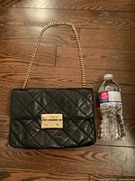 Black quilted leather purse with gold-tone chain and clasp next to a water bottle for scale.