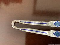 Full view of the beaded necklace showing the white and blue bead pattern with a central diamond design on a dark surface.