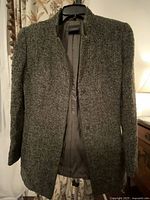 Front view of the boucle jacket showing the charcoal gray textured fabric, collarless neckline, long sleeves, and clean design plastered on a hanger.