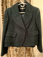 Front view of vintage dark boucle jacket on hanger showing double-breasted buttons and flap pockets