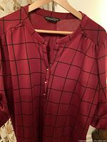 Front view of burgundy Dorothy Perkins dress with black grid pattern, hanging on hanger, showing neckline and buttons.