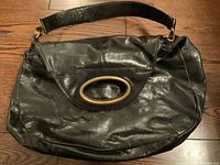 Front view of black leather bucket bag showing brass oval handle, leather shoulder strap, and overall shape and condition of leather.