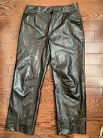 Front view of black leather pants showing the overall condition and shape, highlighting faint gray spots on the lower left leg.