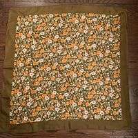 Full view of vintage Liberty of London silk scarf laid flat showing floral print and olive green border.