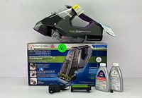 BISSELL Pet Stain Eraser PowerBrush unit placed on top of its original box, alongside battery charger, extra brush, and two bottles of cleaning solution.