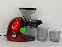 Front view of red SIFENE cold press juicer with black plastic hopper and outlet, two clear plastic containers in front.