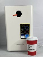 Front view of the white Jafanda air purifier next to a red cup for size reference showing air quality rating labels and brand name.