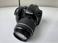Front perspective of black Pentax K-50 camera body with attached DA L 50-200mm f4.5-5.6 ED WR telephoto zoom lens
