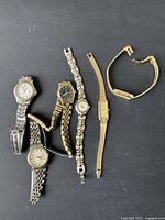 Lot of five women's vintage watches with metal link bracelets in silver and gold tones displayed on black surface.
