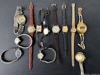 Full lot of 10 women's vintage watches laid out on dark surface showing a variety of watch styles and bands.