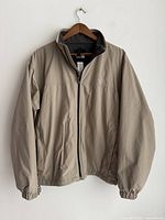 Full view of beige men's jacket on hanger with zipper closed and elastic cuffs visible.