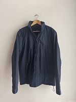 Front view of a navy blue Ralph Lauren Polo jacket hanging on a wooden hanger with visible full front zipper and side pockets.