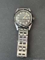 Front view of vintage Timex Electric watch showing round black dial, white numerals and hour markers, metal wristband, and the bezel.