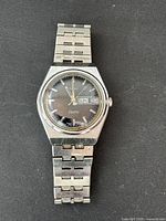 Front view of men's vintage Timex Electric watch showing black dial, day-date windows, and metal link band.