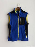 Blue fleece vest with black and yellow accents displayed hanging on wooden hanger against white wall, front view showing full zip and chest pocket with RLX logo.