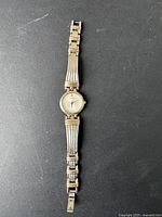 Full view of women's Seiko wristwatch laid out showing silver and gold-tone metal expandable bracelet with fold clasp, round watch face with white textured dial.