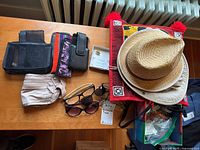 Photo of assorted eyeglasses, sunglasses, cases, wallets, hats, and sewing supplies laid out on a wooden surface