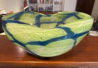 Front angle view of the handmade art glass bowl showing green color with blue swirls and textured details on the surface.