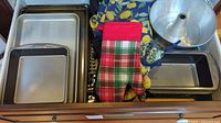 Wide shot showing a drawer with multiple metal baking trays, cooling racks, oven mitts, and the bundt pan