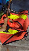 Photo showing an orange high visibility vest with yellow reflective strips, orange tape roll, and walking pole with wooden handle.