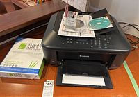 Canon MX532 printer with extra black ink cartridge, CDs, and a ream of copy paper on a table