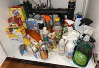 Full view of the assortment of cleaning supplies under sink showing bottles, boxes, brushes and sponges.