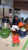 View of the Mr. Coffee coffee maker with two coffee grinders and assorted teapots and kitchenware items on a counter.