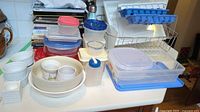Photo of multiple plastic storage containers, ramekins, thermos, cookbooks, and kitchen items on a white countertop.