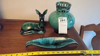 Set of three decorative pottery pieces: deer figurine, vase, and leaf-shaped dish on wooden table with measuring tape for scale.