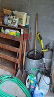 Full view of the lot showing galvanized aluminum bin, garden shovels, gardening sprays, and various tools beside a wall.