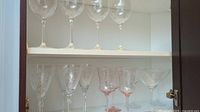 Photo showing upper and lower shelf with various clear and pink-colored vintage crystal stemware including wine glasses and martini glasses.