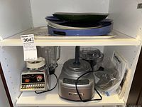 View of all items on shelf showing Cuisinart food processor base, blender, instruction manual, and plates on top shelf