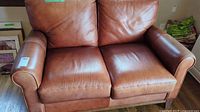 Front view of tan leather loveseat showing two seat cushions and rolled arms.
