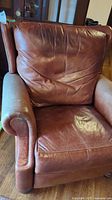 Front view of brown leather recliner showing seat cushion and backrest with creases and signs of wear
