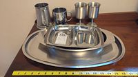 Full set of metal and stainless steel serveware including mugs, goblets, divided dish, and trays with measuring tape for scale.