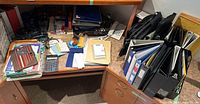 Full view of office desk with assorted office supplies including binders, papers, calculator, headphones.