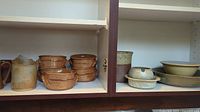 Shelving unit with stacked small brown pottery bowls, a jug, and various other ceramic bowls and dishes in earthy tones.