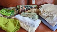 Photo showing varied folded table linens including floral and solid colored pieces with different fabrics and textures.