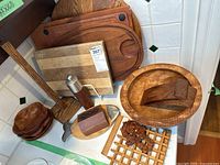 Wooden serving trays, cutting boards, small wooden bowls, a wooden pepper grinder, napkin holder, wooden fish-shaped decorative item, and a wooden lattice trivet on a white counter.
